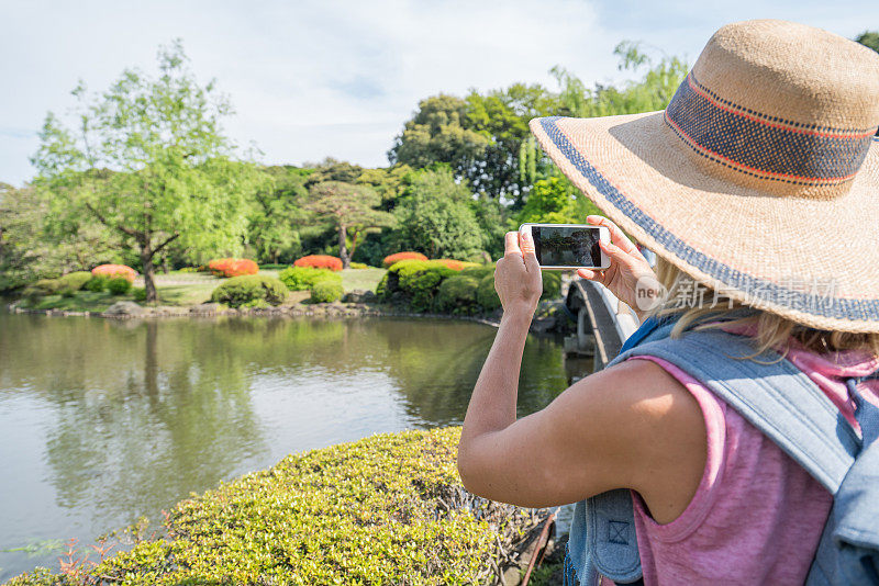 一名年轻女子在东京的日本花园用手机拍照