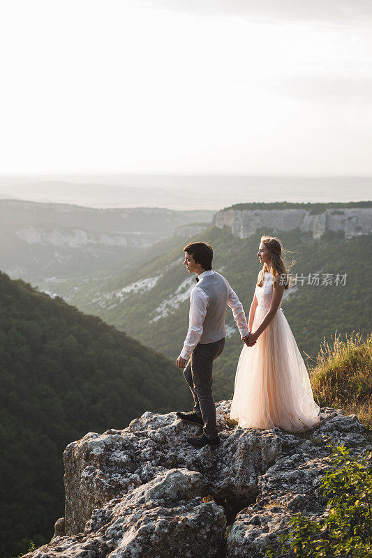 一对新婚夫妇站在悬崖边，欣赏着令人难以置信的美景