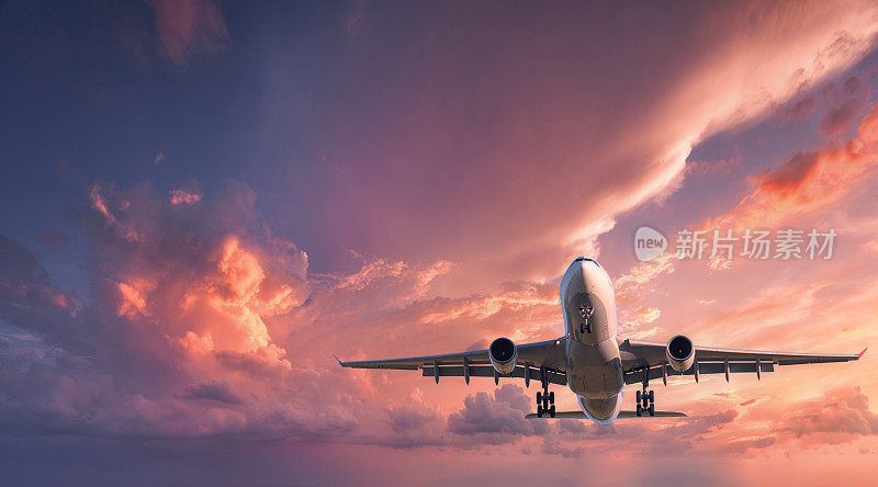 飞机着陆。日落时分，一架白色的客机在布满彩云的红色天空中飞行。旅游的背景。客运班机。商务旅行。商用飞机。私人飞机