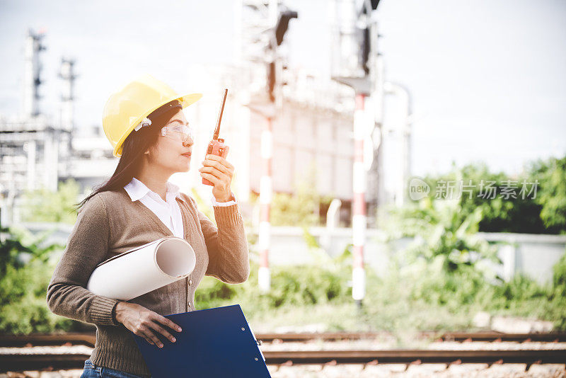 女工程师拿着无线电，蓝图并向发电厂能源工业的工人报告安全控制的时间表。工程师的概念
