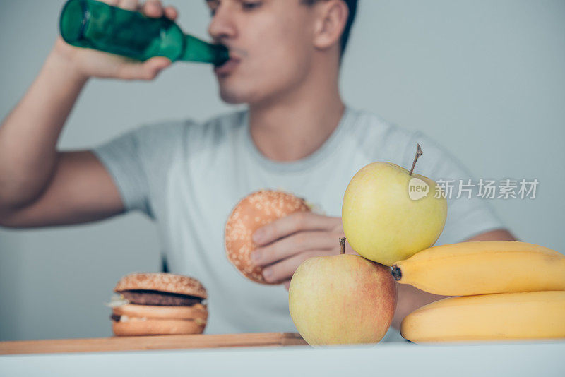 一个人喝着苏打水，吃着汉堡，而水果就在他面前