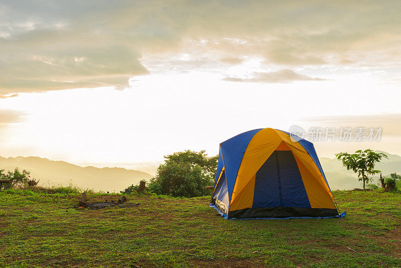 日出时分，游客和帐篷在山上的草地上露营。