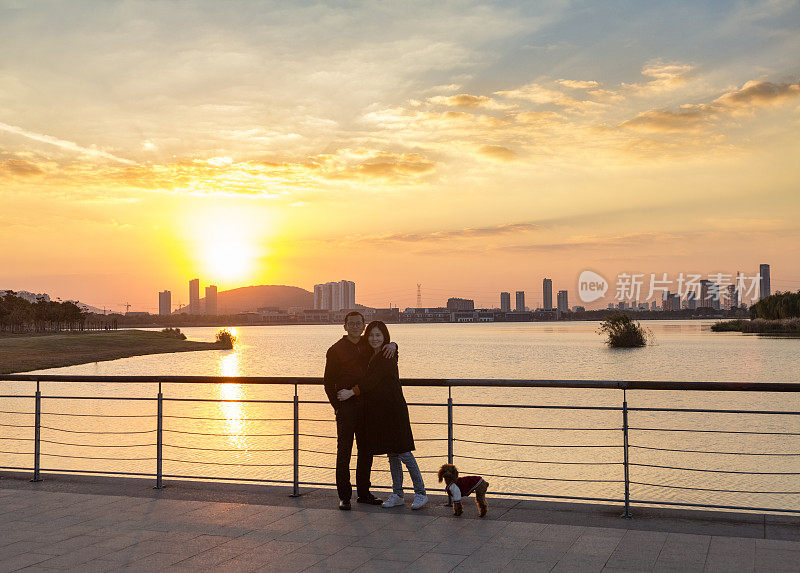 年轻夫妇和他们的小狗对着日落的天空摆姿势
