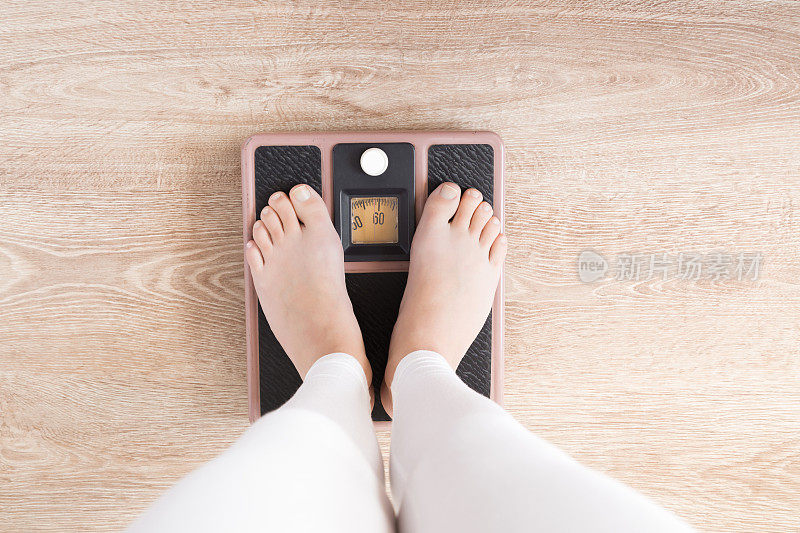 光着脚站在磅秤上的女人。健康营养、瘦身瘦身、减肥新开始。关心身体概念。前视图。