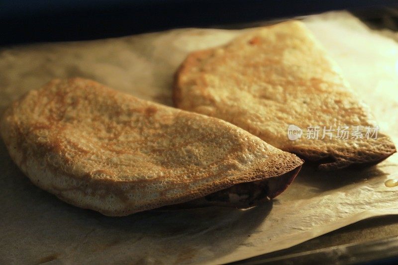 美味的煎饼夹着融化的奶酪，在烤箱里烤着，烤着，涂在防油纸上，呈金黄色