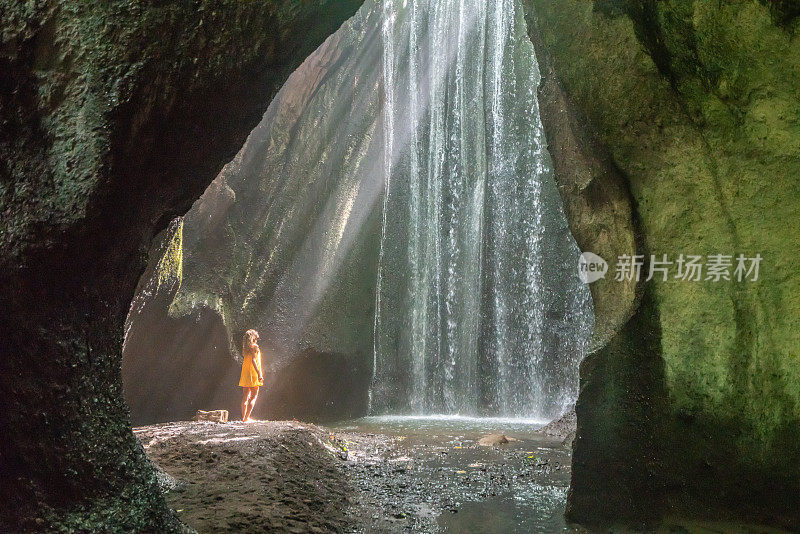 穿着黄色衣服的女孩站在热带雨林的洞穴里，仰望着从岩石上射下来的壮观的阳光。人们旅行的奇妙欲望自然的概念