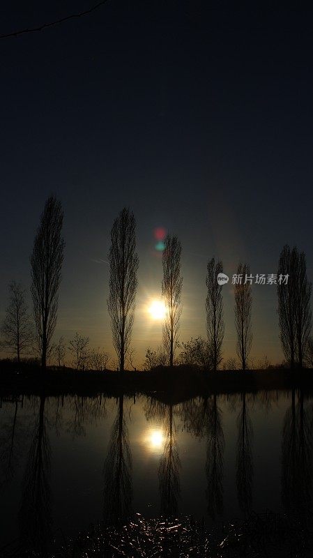 夕阳西下，树木倒映在湖面上