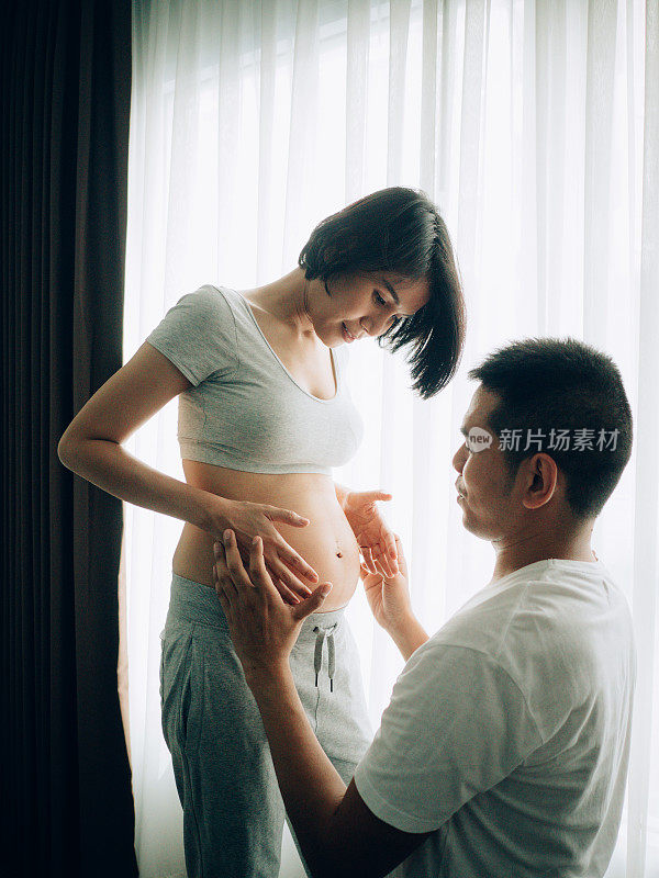 亚洲怀孕夫妇触摸和听肚子在客厅在家里。