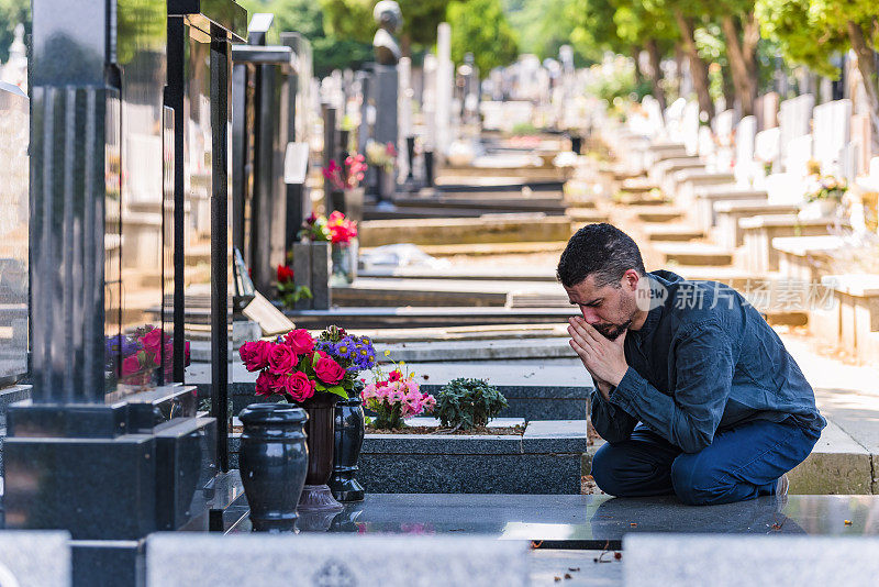 情绪紧张的黑衣男子跪在他家人的墓前