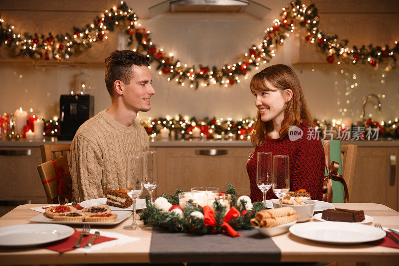 一对年轻夫妇在厨房布置圣诞餐桌。