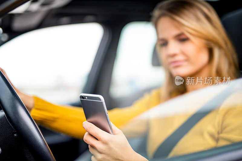 一个年轻女子一边开车一边用手机发短信。