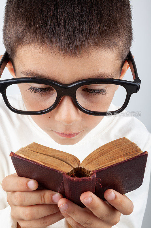 书呆子小男孩戴着大眼镜读一本迷你书