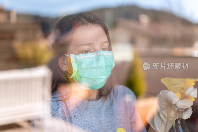 年轻的女孩戴着外科口罩和防护手套在家里擦窗户