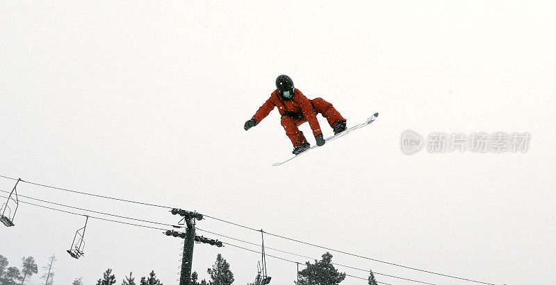 一个滑雪板在完整的冬季装备尝试一个“前侧720静音”在一个跳跃与森林和滑雪跳跃背景在埃尔多拉滑雪度假村附近博尔德，科罗拉多州在一个下雪的，阴天