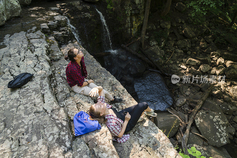 美国宾夕法尼亚州波科诺斯，上黑涡流，两个十几岁的女孩在丁岩瀑布附近的岩石顶部休息