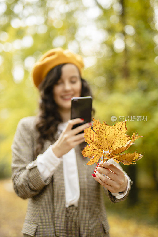 一个女人正在用她的智能手机给秋叶拍照