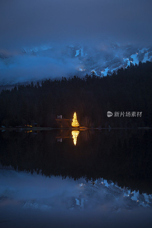 圣诞树灯倒映在湖与山景。