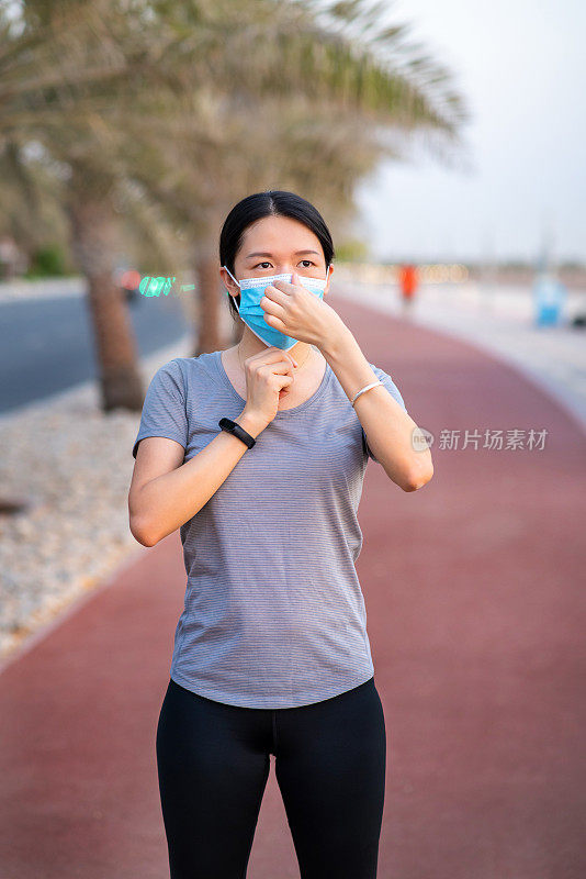 一名妇女在跑步跑道上慢跑前调整外科防护口罩，以防止冠状病毒的传播