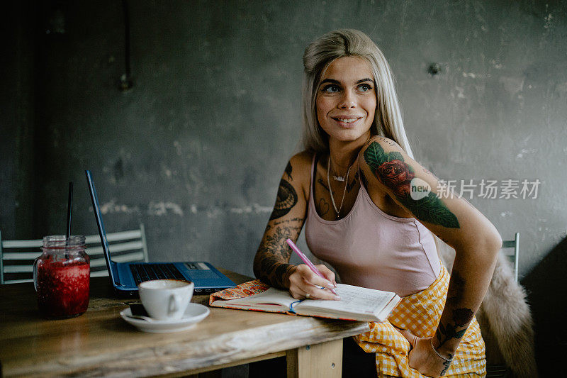 有纹身的年轻女子在咖啡厅用笔记本电脑写字