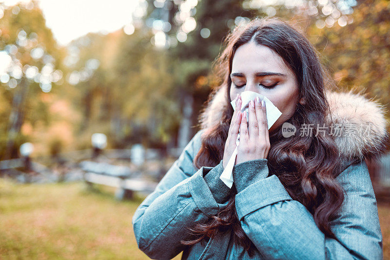 一位女性在一个寒冷的秋天的早晨用纸巾擤鼻子