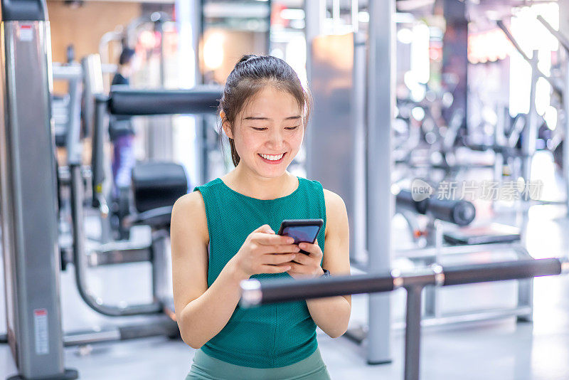 年轻的亚洲女性在健身房使用智能手机
