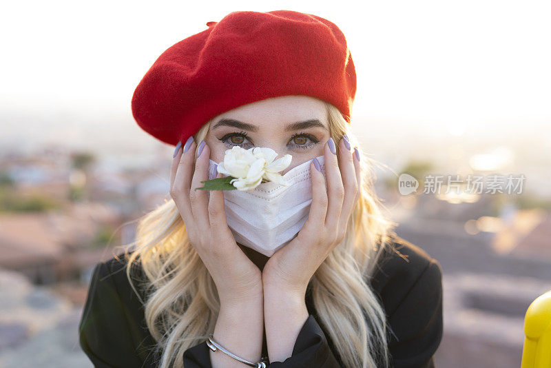 戴着红色贝雷帽的金发女人拿着白玫瑰。带花的面膜设计。美女肖像