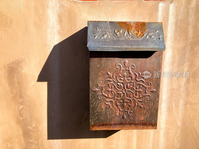 圣达菲风格:生锈的阳光下的老式邮箱在土坯墙上