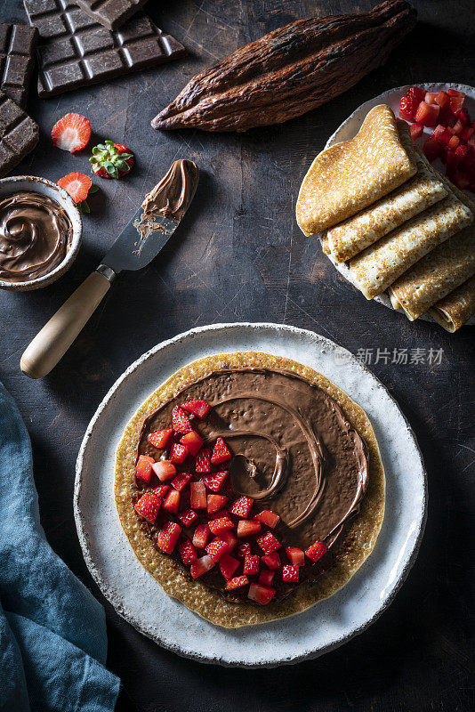 可丽饼素食Crêpes与可可奶油巧克力涂抹和草莓在深色木材的背景