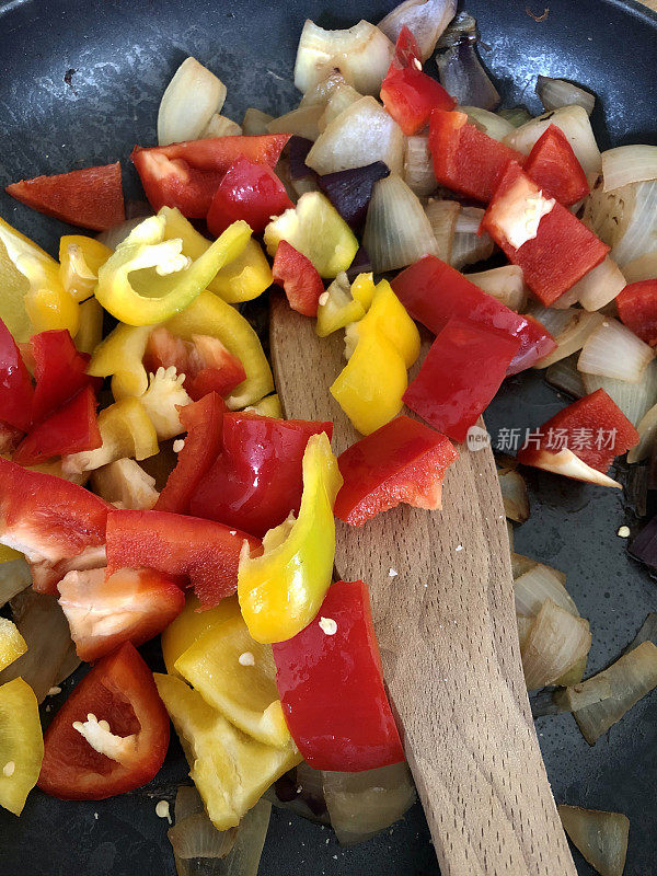 木勺在不粘锅里翻炒蔬菜，用红黄椒和红白洋葱丁烹饪，高视化的画面