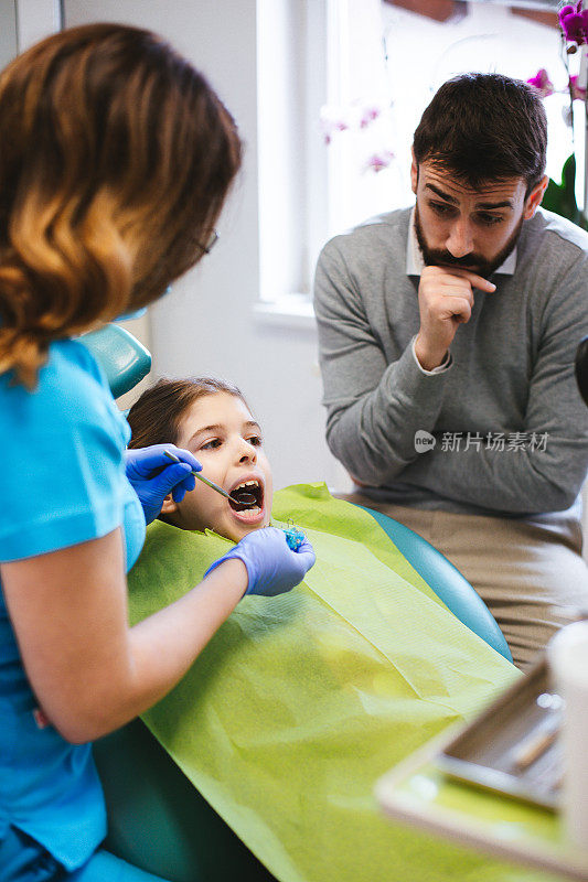 当牙医在检查她的牙齿时，女儿坐在牙科椅上。