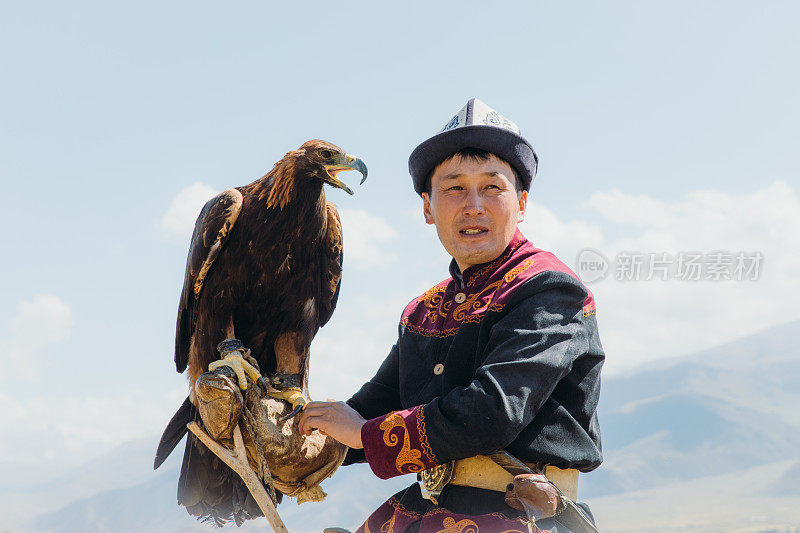 在中亚山区，身穿传统服装的老鹰猎人和老鹰在一起