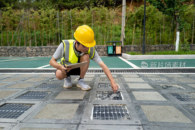 技术人员蹲下来检查安装在停车场地面上的太阳能电池板的损坏情况