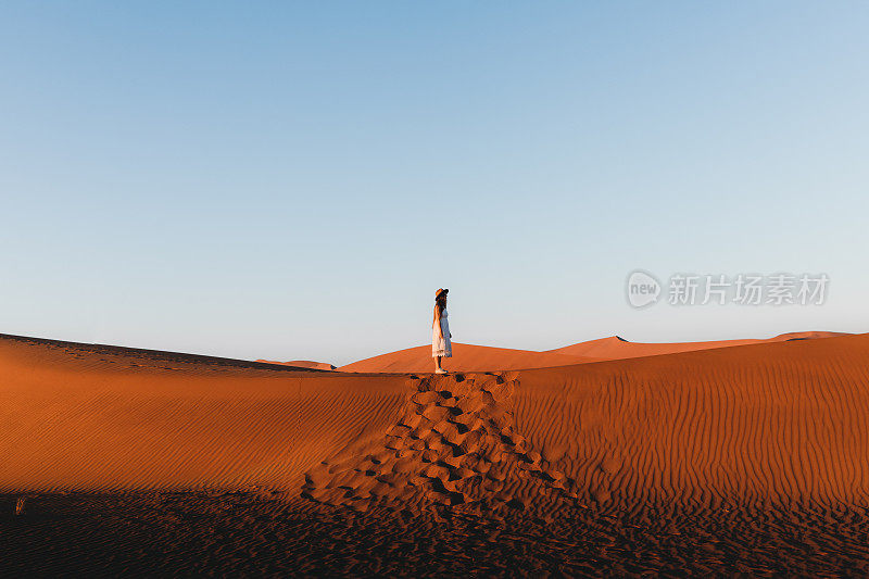 穿着衣服和帽子的女游客在纳米比亚索苏瓦莱的日出期间探索风景秀丽的沙丘