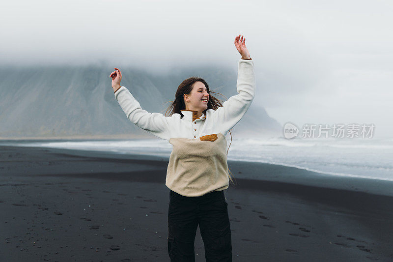 年轻女子旅行者在郁郁寡欢的黑沙滩与山景