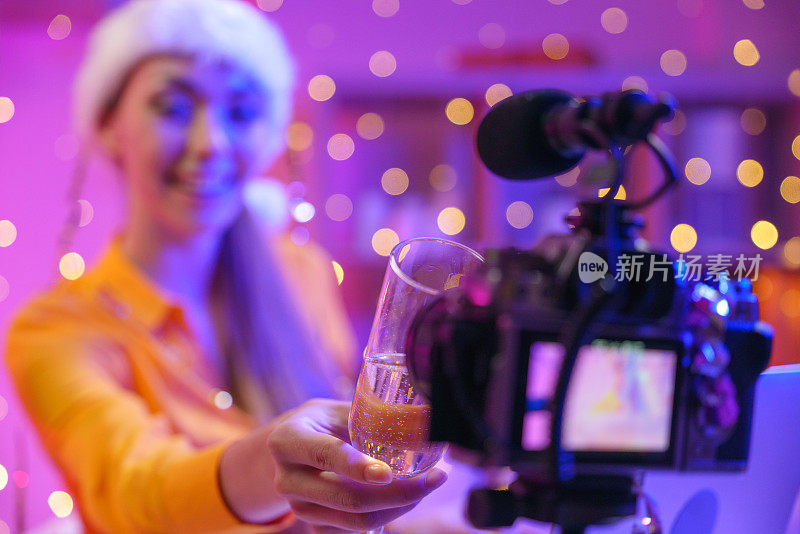 视频博主女孩轻轻地用香槟杯对着摄像机碰杯。
