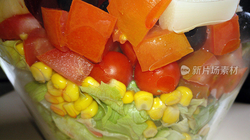 生菜叶子，玉米和西红柿片放在一个玻璃碗里，背景是沙拉。