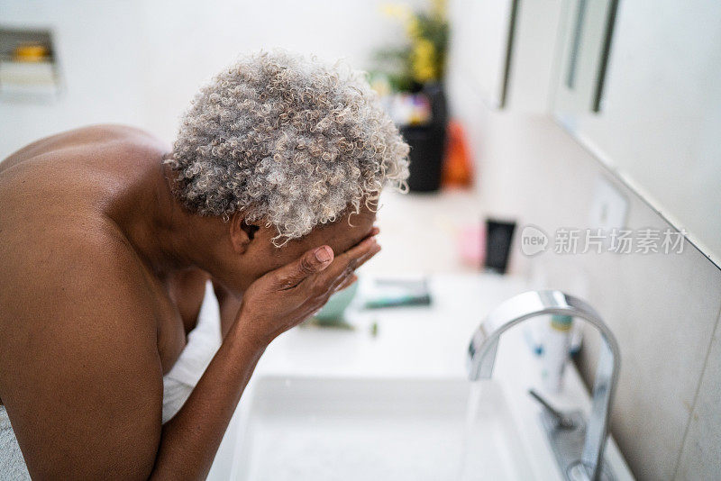 一位年长的女士在家里的浴室里洗脸