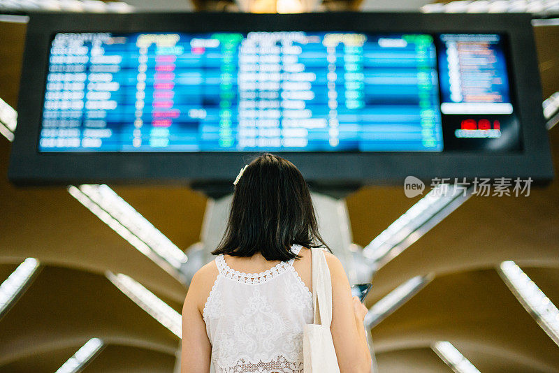 亚洲女游客在看机场的到达和离开指示牌