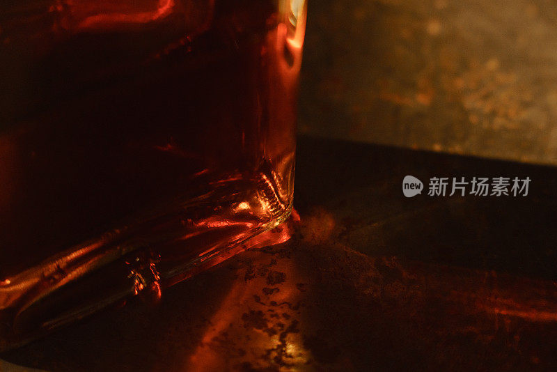 一个威士忌酒瓶的近距离微距照片，阳光通过。烈性酒精使阳光折射，在桌子上产生美丽的焦散效果。