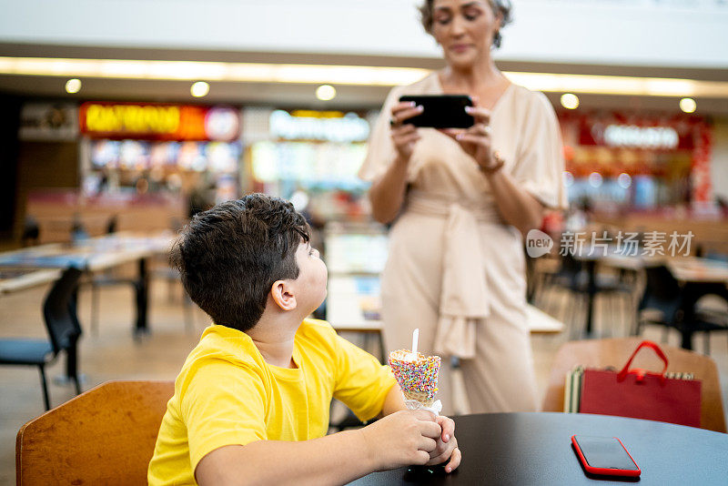 母亲拍摄或拍摄她的儿子在美食广场吃冰淇淋