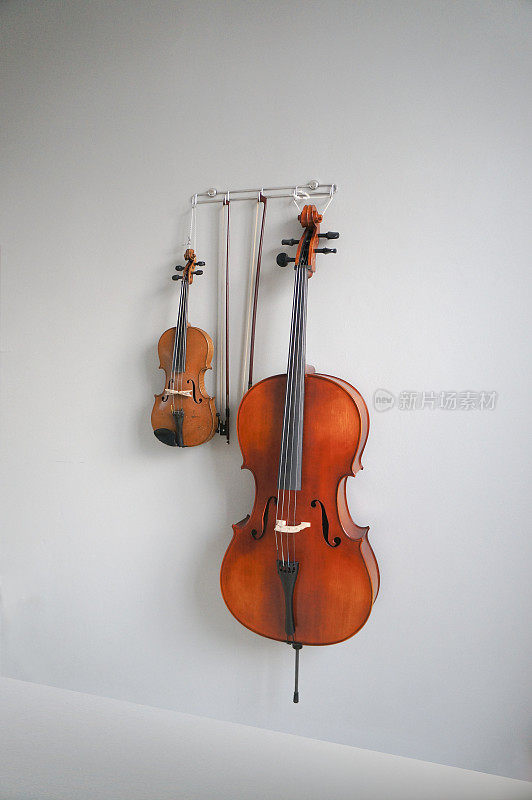 灰色梯度墙上挂着小提琴、大提琴和弓。