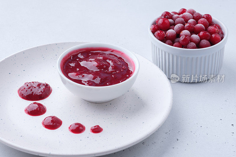 新鲜的有机蔓越莓酱和蔓越莓在白色的小杯背景。