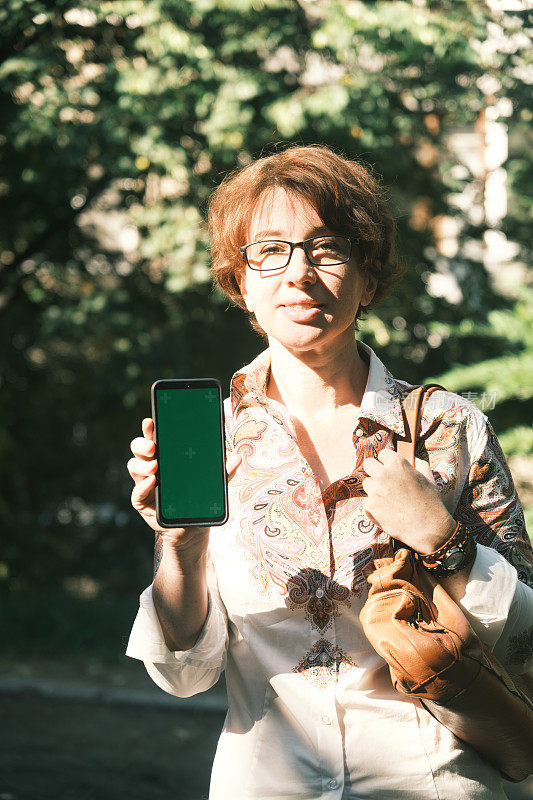 开朗成熟的女人在她的智能手机上显示绿色屏幕