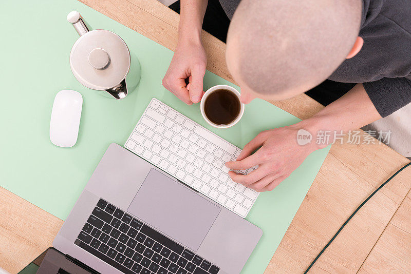 顶视图的照片，一个秃顶的人在笔记本电脑上工作，在桌子上喝茶。创造力。设计师。发展。就业。小工具。灵感。的工作。学习。茶壶。的概念。互联网。在线