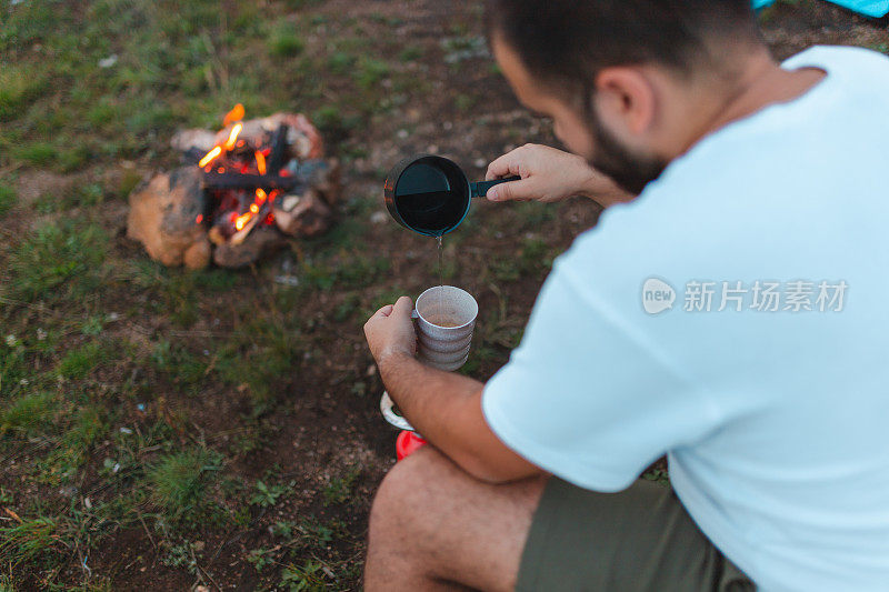 一个年轻的男性徒步旅行者在篝火旁用野营炉煮咖啡的特写