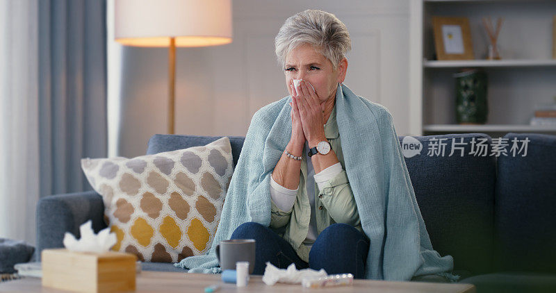生病，流感和生病的老年妇女用纸巾擦她的鼻窦，生病和打喷嚏的毯子在家里。老年女性不开心，独自一人，感冒伴新冠病毒或发烧坐在客厅沙发上。