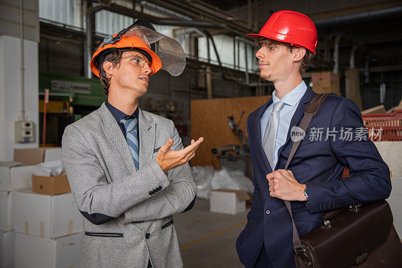 两名同事在工厂工作时交谈，工程师穿着优雅戴着防护头盔。