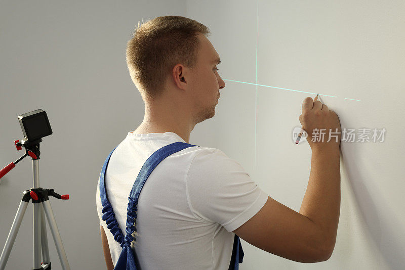 工人使用交叉线激光水平仪和铅笔对光壁进行精确测量