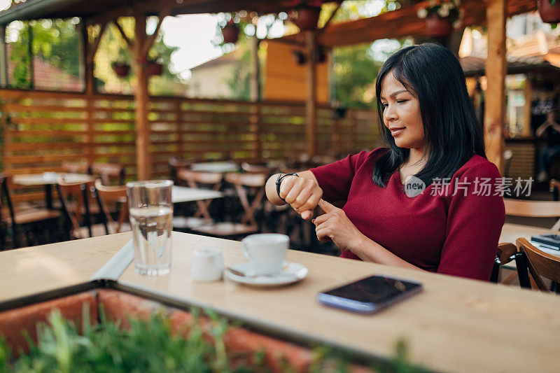 穿着便装的女交易员在咖啡店里喝着咖啡，用着智能手表