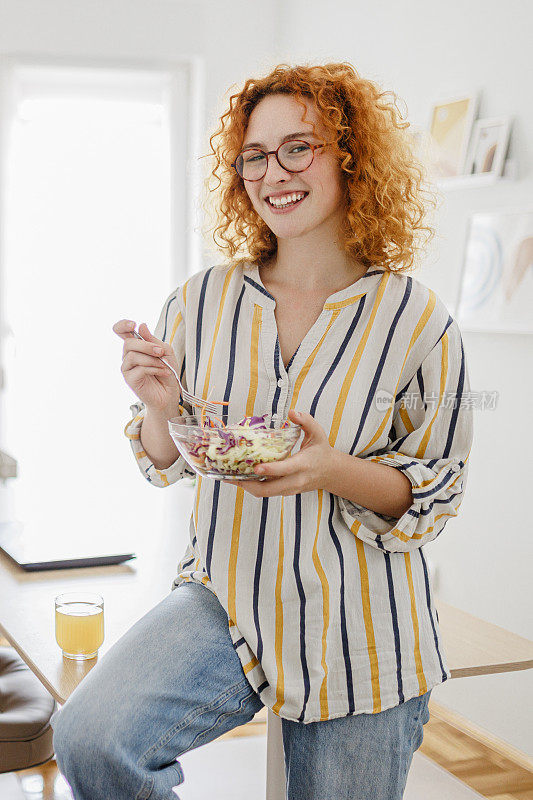 一个快乐的年轻女人在家吃沙拉的画像